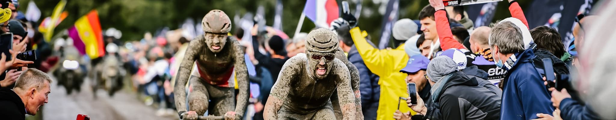 Mud-covered cyclists racing, fans cheering
