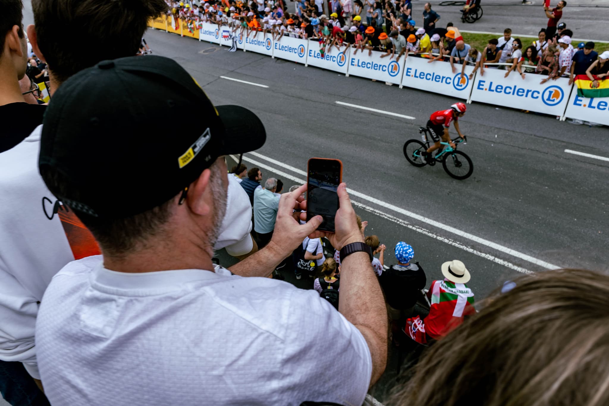 Cyclist in red jersey racing past spectators at Tour de France stage finish.