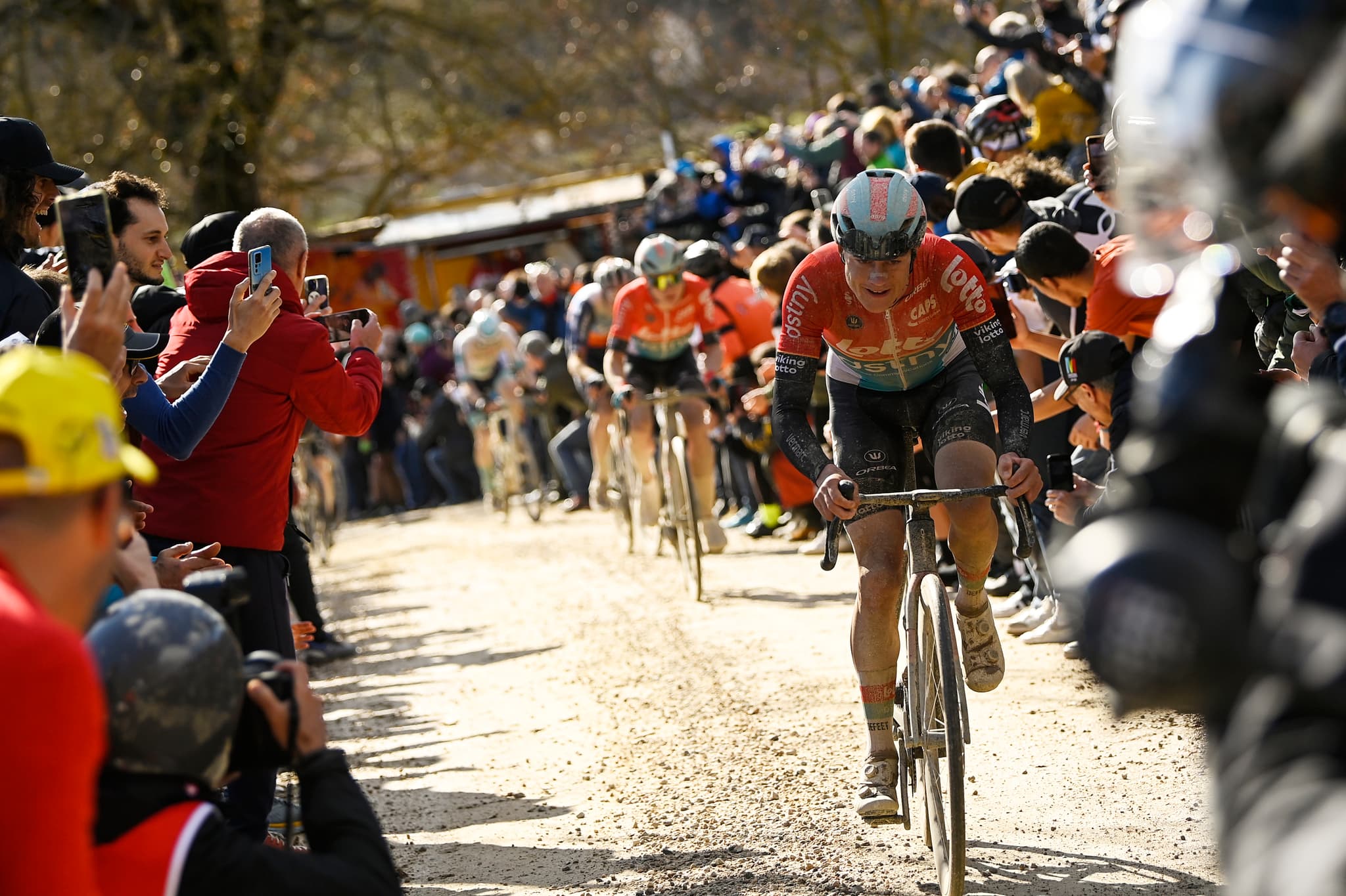 Lotto Dstny rider on Strade Bianche gravel, spectators line the road.