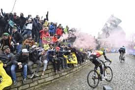 Cyclists on cobbled road with crowds and smoke